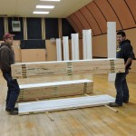 two men carrying a stack of 6 lightweight trade show panels high strength cam lock panels